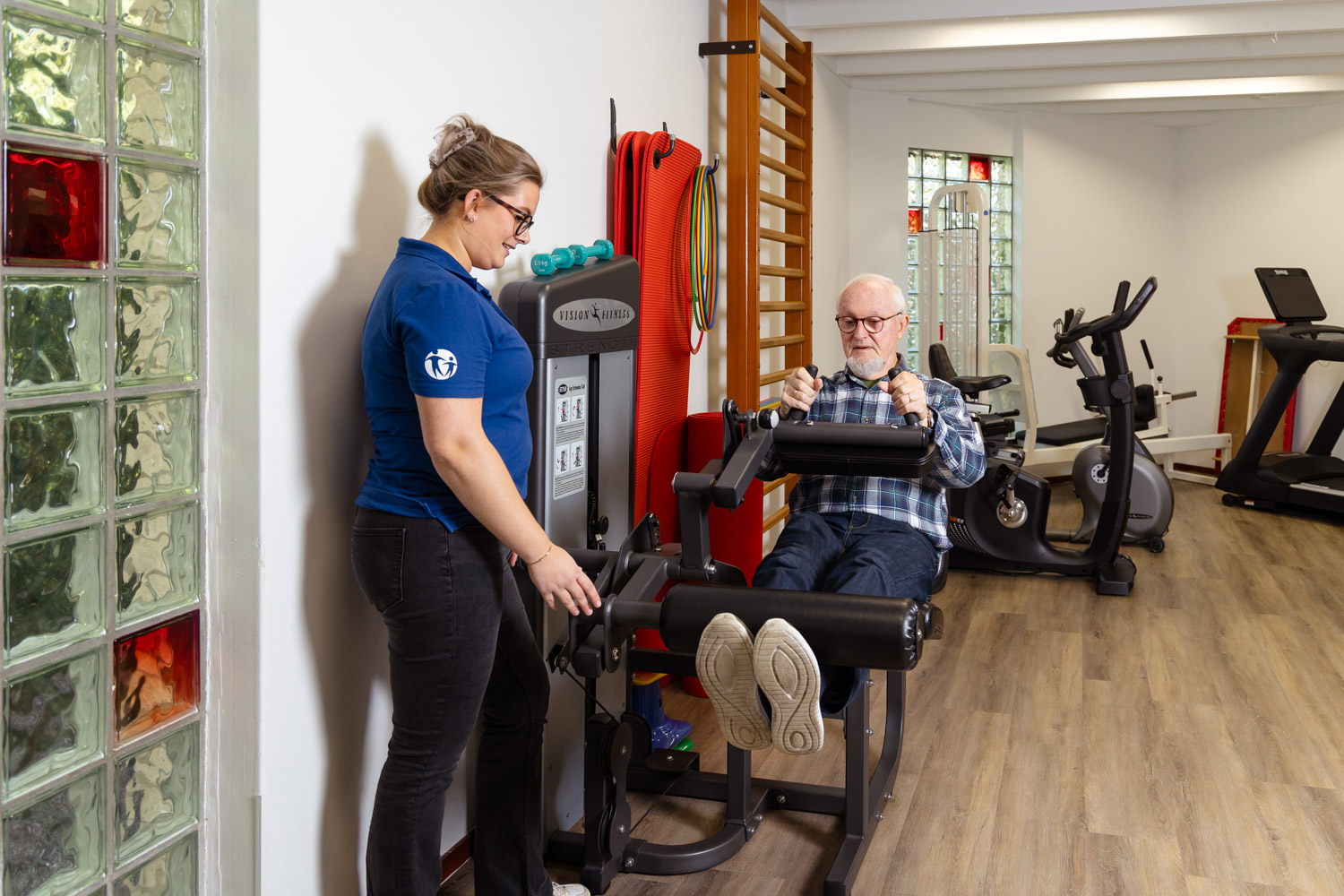 patient zit op een toestel en wordt geholpen door de fysiotherapeut