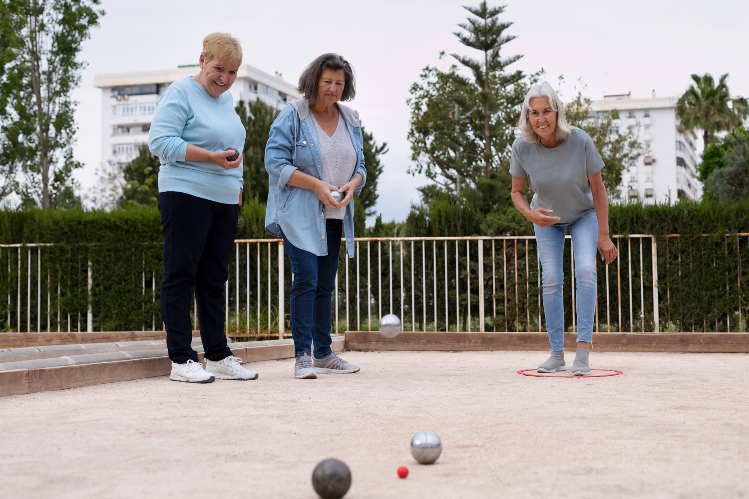 Drie oudere vrouwen zijn aan het sporten. Ze spelen Jeu de Boules op een pétanqueveld.